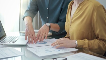 Team collaboration over financial reports. Close-up view of two business people, professionals analyzing financial charts and data on a desk near a laptop computer