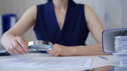 Fototapeta premium Businesswoman holding magnifying glass analyzing financial documents at office desk. Taxes, audit in business