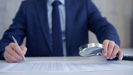 Businessman is carefully examining financial documents with a magnifying glass, highlighting the importance of thorough analysis in business. Audit and taxes