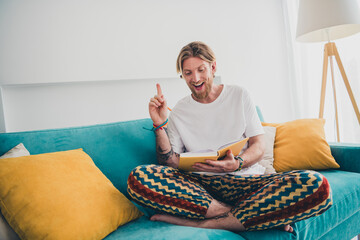 Full length photo of attractive young male sit couch read book excited idea eureka dressed...