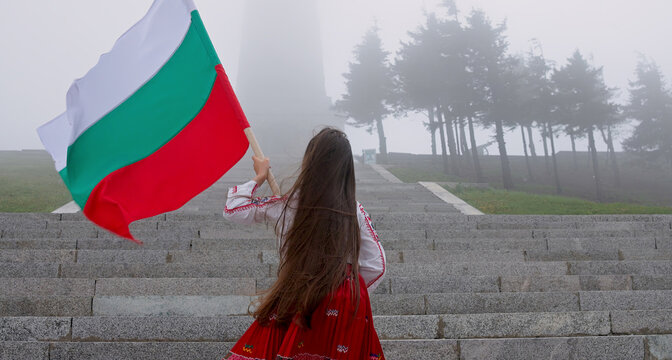 Woman in ethnic folklore costume with Bulgarian flag climbing Shipka monument, celebrating independence of the country