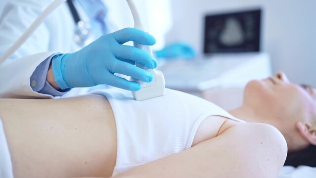 Doctor man, wearing blue medical gloves, is using ultrasound machine to examine internal organs of a patient woman, close up vie. Female mammary gland health. Medicine