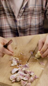 man peeling fresh garlic on wooden cutting board in kitchen
