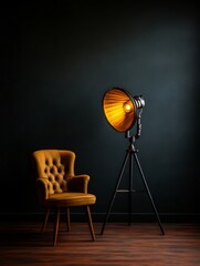 A vintage tripod lamp with an extended bellows casts a warm glow on a leather armchair in a dark, moody setting. The lamp's industrial design adds a touch of vintage charm, while the armchair provides