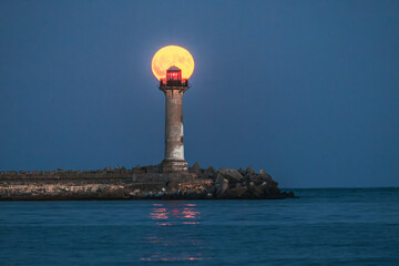 Lighthouse beacon and full moon twilight over sea horizon and moonlight in ripple water