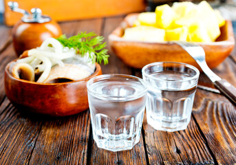 one empty second vodka-filled glass surrounded by a snack with herring and onions
