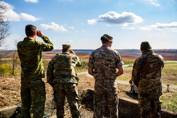 Four soldiers are standing in a field, looking at something in the distance © Joshua