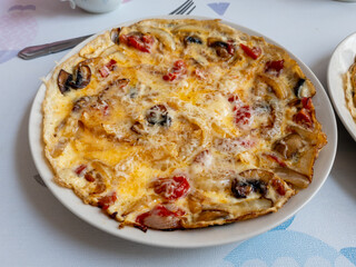 An open or flat omelette with tomatoes, mushrooms, onions and cheese, served on a plate.