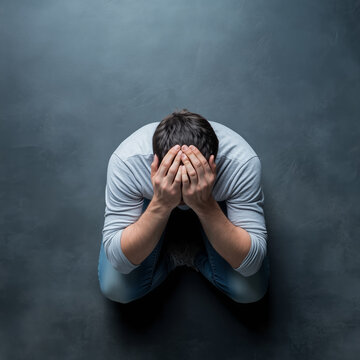 Man sitting on the floor, head in hands, expressing despair