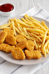 Fried Chicken Nuggets with French Fries on a Plate, side view.