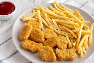 Fried Chicken Nuggets with French Fries on a Plate, side view.