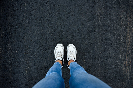 Female feet in white sneakers standing on street asphalt