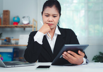 Businesswoman in black suit using digital tablet and working on laptop computer on table at office. Businesswoman finger touching on tablet screen at desk and suring the internet, close up