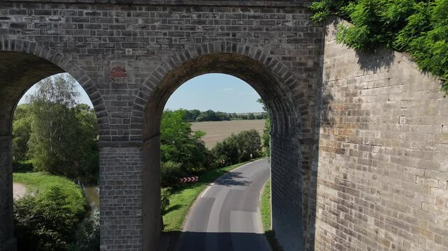 Przelot drony z kamerą pod wiaduktem kolejowym nad przyjeżdżającymi samochodami widok z g&oacute;ry, widok z lotu ptaka.