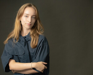 A woman with long blonde hair wearing a loose blue shirt is posing with a serious expression in a professional studio setting with a dark grey background.