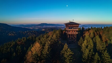 Obraz premium A wooden watchtower atop an old forest in the mountains, a drone's-eye view with mountains and a flat valley behind it. Aerial photography, a telephoto lens on a sunny day.