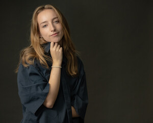 A studio portrait of a young blonde woman in a blue shirt posing thoughtfully with her hand on her...