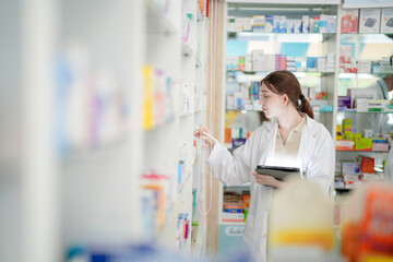 Obraz premium woman pharmacist checks and arranges medicines on pharmacy shelves, emphasizing precision and responsibility in healthcare services. The scene highlights the daily operations in a modern pharmacy.