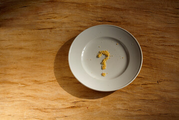 Bread crumbs forming a question mark on a plate. Hunger,inequity and poverty concept. Close up with free copy space.