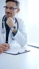 Obraz premium Doctor and a patient. The physician, wearing a white medical coat over a green shirt, gesturing with his hands during a consultation in the clinic. Medicine concept