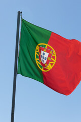 National flag of Portugal waving gracefully against a clear blue sky. The flag's vibrant red and green colors symbolize Portuguese pride and heritage, making it a powerful national symbol