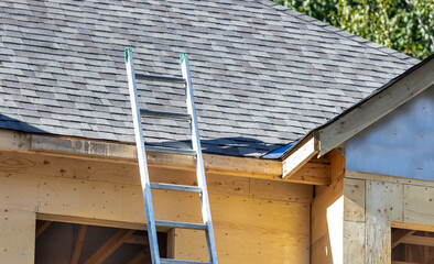 An aluminum extension ladder leaning against the roof of a house under construction © SockaGPhoto
