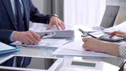 Business people wearing blue suits are reviewing financial data in office. Male auditor is using a magnifying glass. Audit and taxes concept