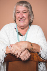 Beautiful looking senior elderly woman aged 70+ smiling cheerfully sitting on a wooden chair. Happy mature woman with short grey hair laughing