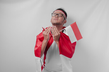 Serious Indonesian man wearing jersey with flag draped over shoulder doing praying gesture.