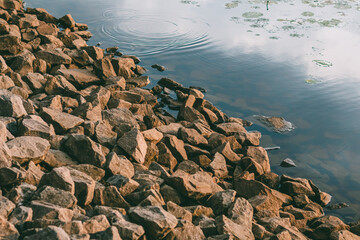 Stone sloped descent to the river water in the rays of the sun at sunset. Granite stones of...