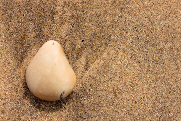 Tear-drop shaped stone sits on the sand at Kohler-Andrae State Park, Sheboygan, Wisconsin in late August or heart-shaped when rotated