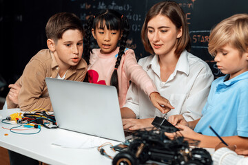 Teacher coding to demonstrate children how to code robots in the STEM class. Children fun to watch how teacher coding with confident only boy in blue shirt taking note with serious look. Erudition.