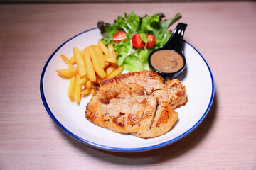 Chicken steak with side dishes of French fries, salad and pepper sauce on a white plate, photographed with studio lights.
