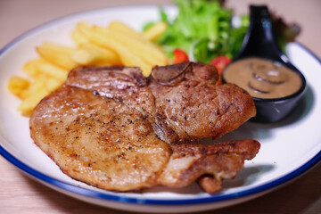 Pork chop steak with side dishes of French fries, salad and pepper sauce on a white plate, photographed with studio lights.