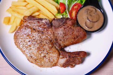 Pork chop steak with side dishes of French fries, salad and pepper sauce on a white plate, photographed with studio lights.