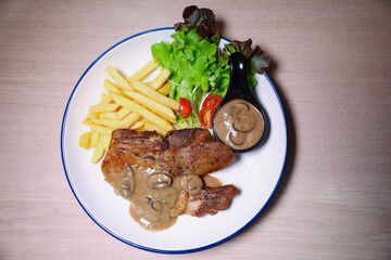 Pork chop steak with side dishes of French fries, salad and pepper sauce on a white plate, photographed with studio lights.