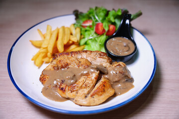 Chicken steak with side dishes of French fries, salad and pepper sauce on a white plate, photographed with studio lights.