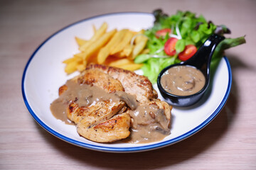 Chicken steak with side dishes of French fries, salad and pepper sauce on a white plate, photographed with studio lights.