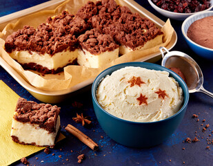 A rich cheesecake topped with chocolate crumble, served alongside a bowl of whipped cream with star decorations.