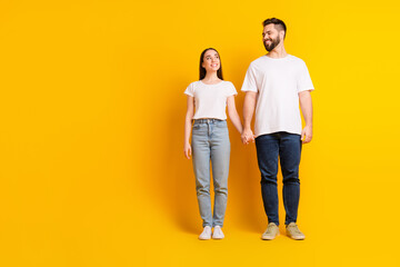 Fototapeta premium Full body photo of attractive young man woman look each other hold hands dressed stylish white clothes isolated on yellow color background