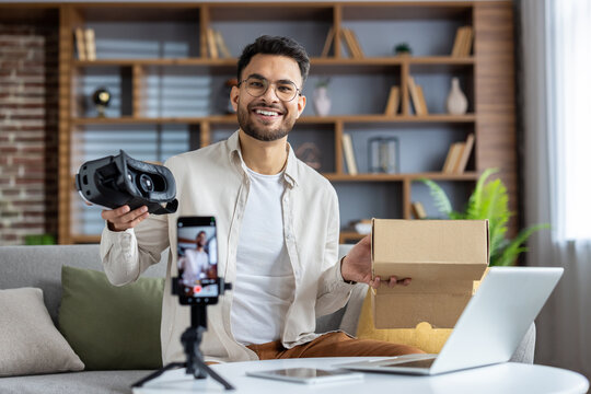 Smiling man creating unboxing video with smartphone as he showcases virtual reality headset in home setting