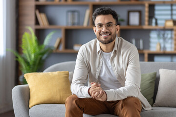 Smiling man sitting comfortably on sofa in modern living room interior with cozy and elegant decor