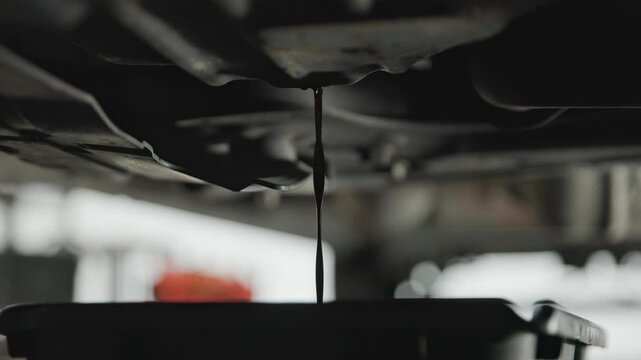 Old and wasted synthetic oil being drained into basin van beneath car and sprinter van garage floor as it pours out in slow motion and close-up into a bucket