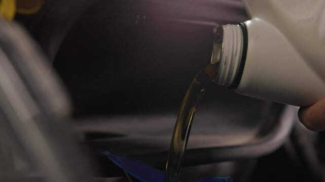 Pouring five quarts of dark synthetic motor oil into gasoline car engine for a sprinter van front out of a white bottle can in slow motion and close-up shot