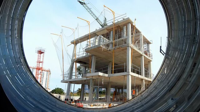 A new building is taking shape at a construction site, showcasing modern architecture and active machinery from a distinct viewpoint. Workers are busy at various tasks.