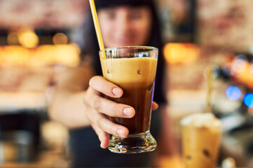 Hand, glass and serving ice coffee, alcohol or cocktail beverage with straw at cafe bar. Closeup, bartender and giving latte to woman for cold brew or drink order at happy hour for hospitality at pub