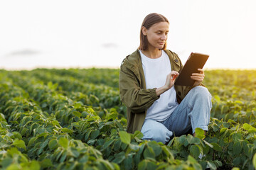 Female farmer uses digital tablet for analyse and check soybeans plants at field. Modern...