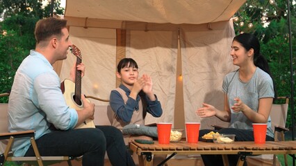 Family together camping. Mother and daughter listening father play guitar. Parent use outdoor camping activity to communicate and spending time with young generation cross generation gap. Divergence.