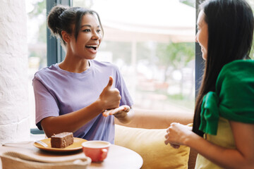 Happy friends, multiracial women using sign language while having coffee at local cafe