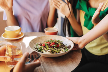 Waitress serving healthy quinoa salad to friends in restaurant, selective focus